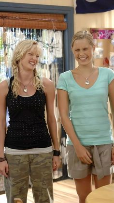 two young women standing next to each other in front of a store window smiling at the camera