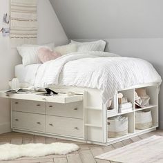 a white bed sitting under a slanted ceiling next to a dresser and drawers in a bedroom