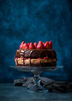 a chocolate cake topped with strawberries on top of a glass platter next to a blue wall