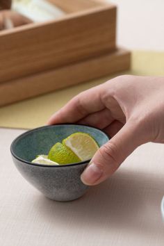 a person holding a lemon in a bowl on a table with chopsticks next to it