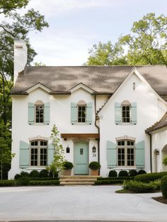 a large white house with blue shutters on the front and side windows, surrounded by greenery