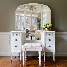 a white vanity with a mirror and stool in front of it on a hard wood floor