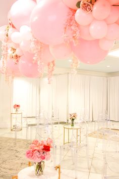 a bunch of pink balloons hanging from the ceiling above a table with chairs and flowers in vases