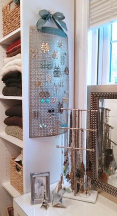 a white dresser topped with lots of jewelry next to a wall mounted necklace holder and mirror