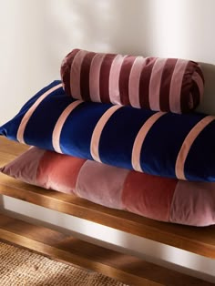 three pillows are stacked on top of each other in front of a white wall and wooden bench