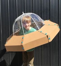 a young boy is holding an open cardboard box with blue beads on it while standing in front of a black wall