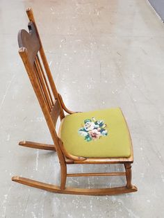 a wooden rocking chair with a flowered seat pad on the floor in a room