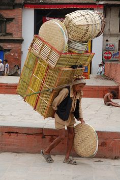 a man carrying baskets on his back down the street