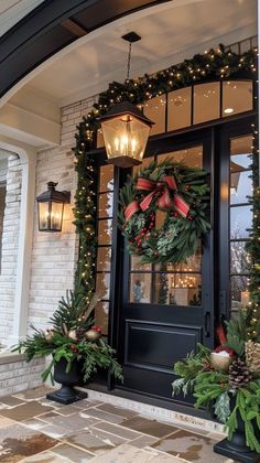 christmas wreaths and lights decorate the front door of a house with holiday greenery