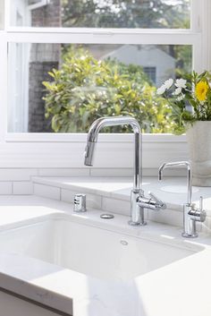 a white kitchen sink sitting under a window next to a vase with flowers in it