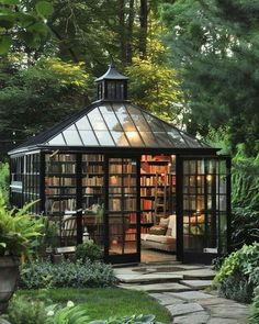 a small glass house in the middle of a garden with lots of trees and plants