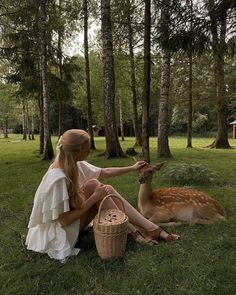 a woman sitting in the grass petting a deer's head with her hand