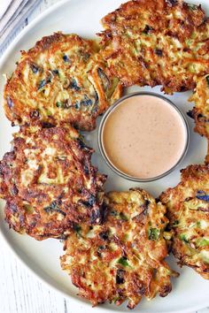 several crab cakes on a white plate with a dipping sauce