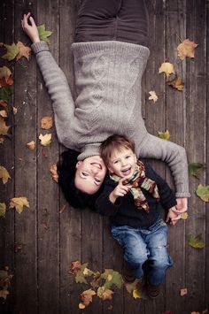 an overhead view of a mother and her child laying on the ground with autumn leaves around them