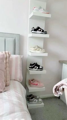 a white bed topped with lots of shoes next to a shelf filled with pink and white pillows