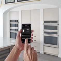 a person holding up a smart phone in a large kitchen with white cabinets and appliances