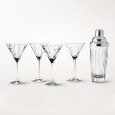 four wine glasses and a cocktail shaker on a white surface