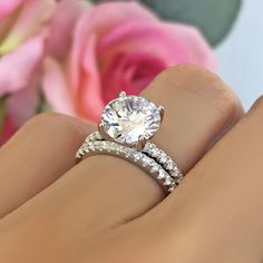 a woman's hand with a diamond ring on top of her finger and pink roses in the background