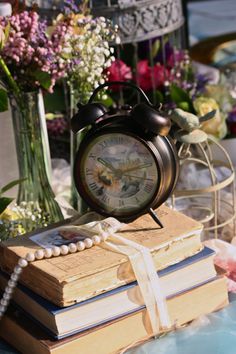 an alarm clock sitting on top of a stack of books with flowers in the background