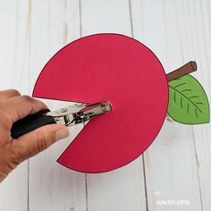 someone cutting out the paper for an apple craft