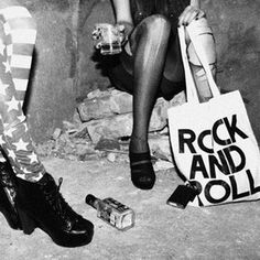 black and white photograph of two women sitting on the ground with their legs crossed, one holding a rock and roll bag