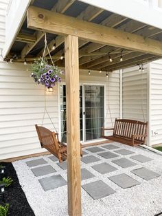 a wooden porch swing sitting on top of a stone floor next to a white building