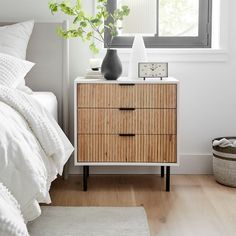 a bedroom with a bed, nightstand and window in the corner that has a plant on it