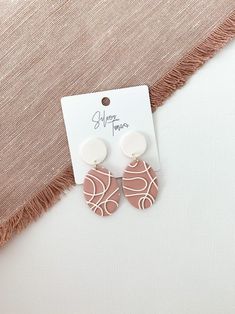 the pink and white earrings are next to a piece of fabric on top of a table