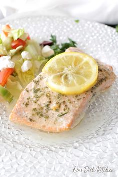 a white plate topped with salmon and salad next to a lemon slice on top of lettuce