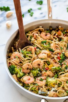 shrimp and broccoli pasta in a skillet with a wooden spoon on the side