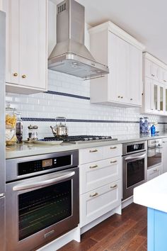 a kitchen with stainless steel appliances and white cabinets, wood flooring, and marble counter tops