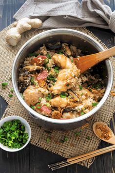 a pan filled with chicken and rice next to some green onions on a wooden table