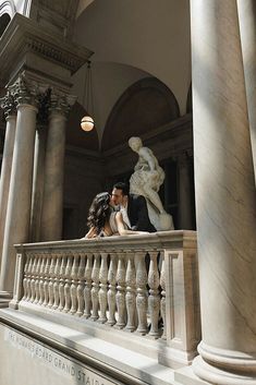 a bride and groom standing on the balcony of a building with columns in front of them