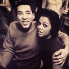 a black and white photo of a man and woman posing for the camera with their arms around each other