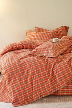 an orange and white checkered comforter set on a bed with two pillows in the corner