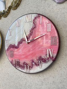 a marble clock with roman numerals on the face and pink paint splattered in gold