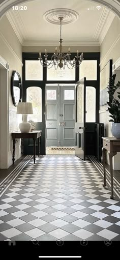 a hallway with black and white checkered flooring, chandelier and mirror