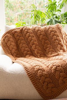 a brown blanket sitting on top of a white couch next to a potted plant