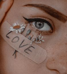 a woman's eye with the word love taped to her cheek and daisies sticking out of it