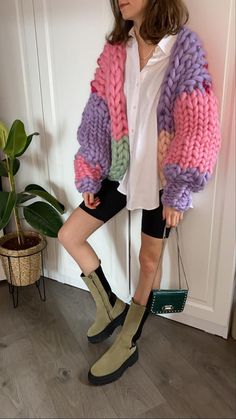 a woman standing in front of a door wearing boots and a colorful cardigan sweater