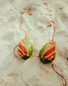 two green and orange balls in the sand with string attached to them, on top of each other