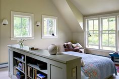 a bed sitting under two windows in a bedroom next to a book shelf filled with books