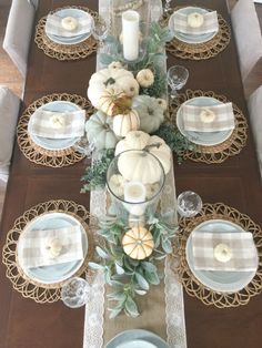 a dining room table set with white pumpkins and greenery