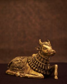 a golden cow figurine sitting on top of a black cloth covered floor next to a brown wall