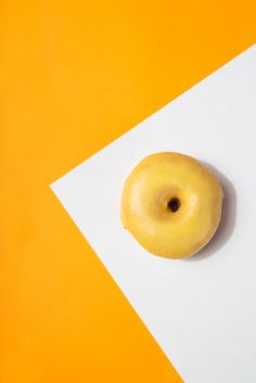 a yellow donut sitting on top of a white piece of paper next to an orange background