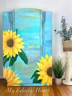 a painting of sunflowers painted on a blue cabinet next to a potted plant