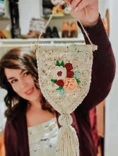 a woman is holding up a crocheted wall hanging