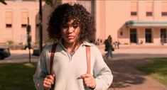 a woman with curly hair standing in front of a building holding onto a brown bag