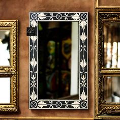 an ornate black and white mirror on the wall next to three gold framed mirrors with decorative designs