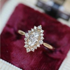 an engagement ring with a pear shaped diamond surrounded by small round diamonds on a red velvet box